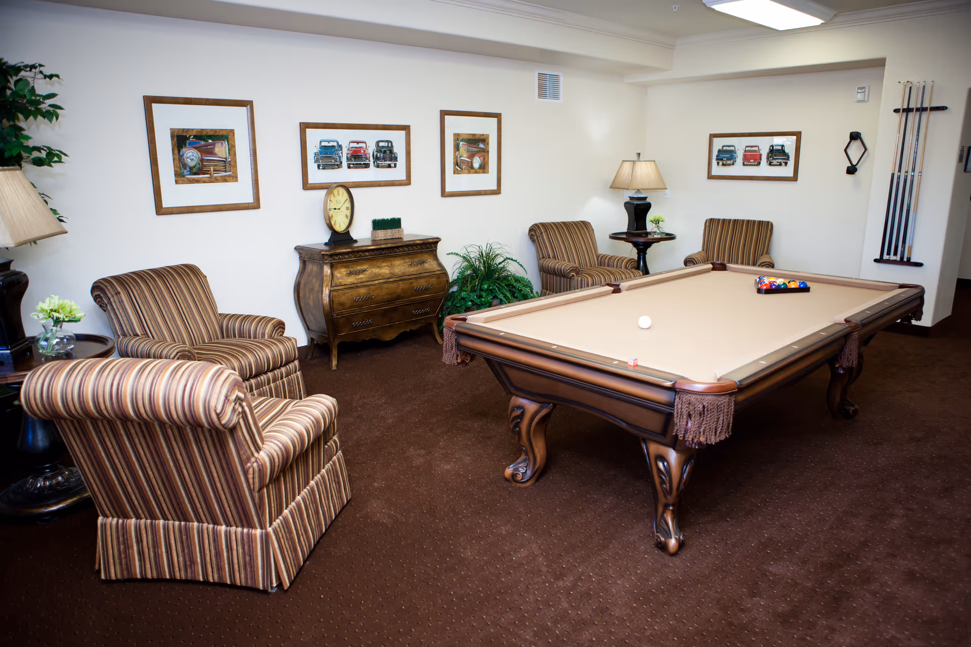 Carpeted lounge with a billiards table, striped armchairs, side tables and framed pictures on the walls.