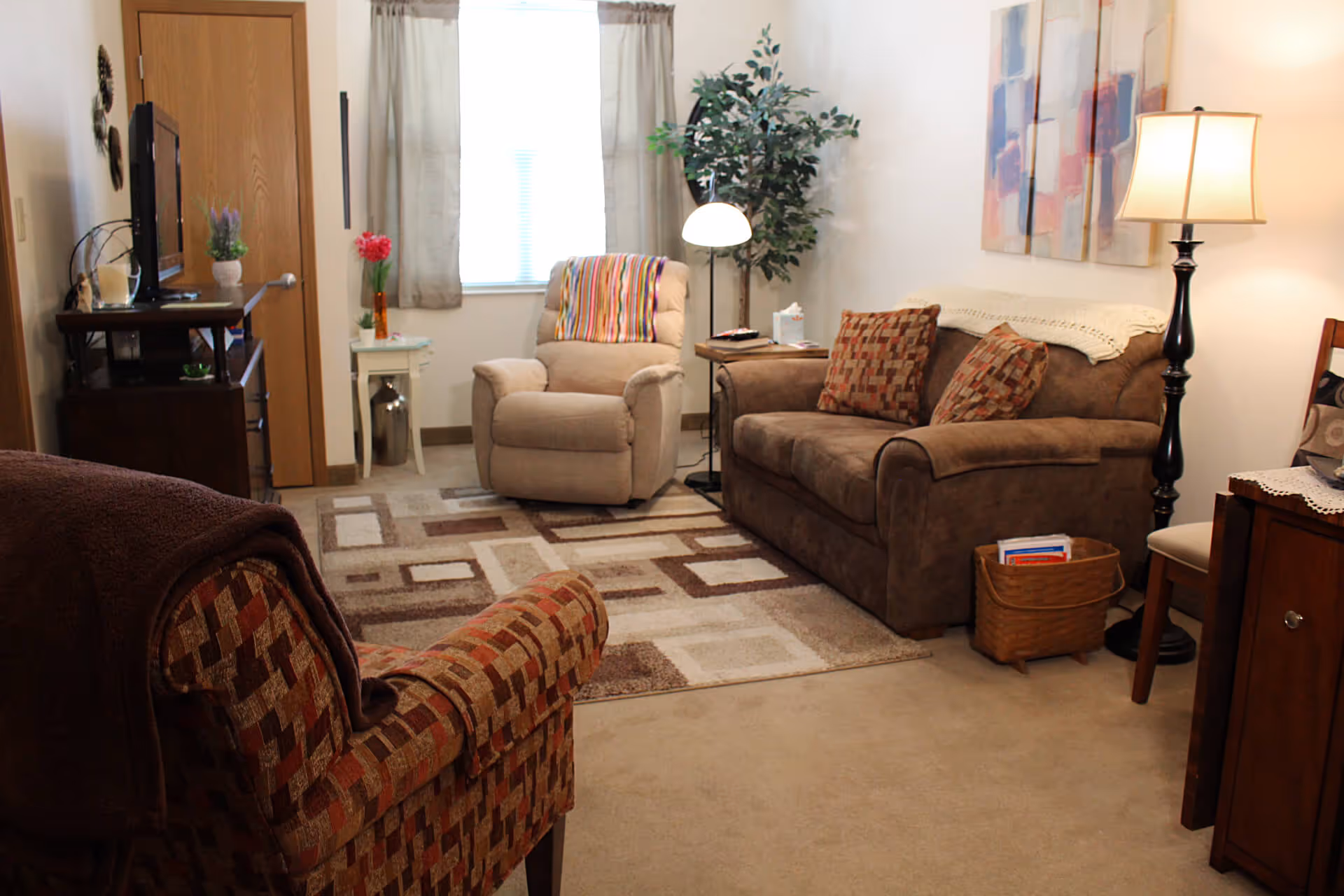 Cozy living room with a sofa, two armchairs, TV on a stand, floor lamp, rug, and decorative plant.