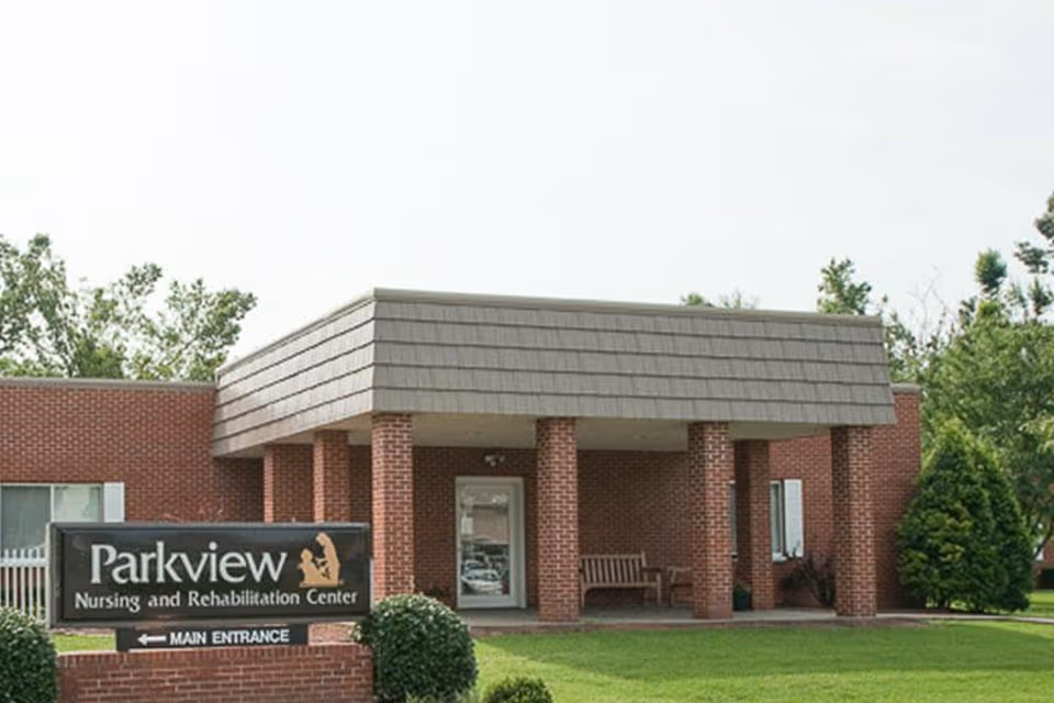 Brick single-story nursing and rehabilitation center entrance with a covered portico and a Parkview sign on the lawn.