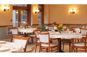 Well-lit dining room with round tables covered in white tablecloths, wooden chairs, floral centerpieces and wall sconces.
