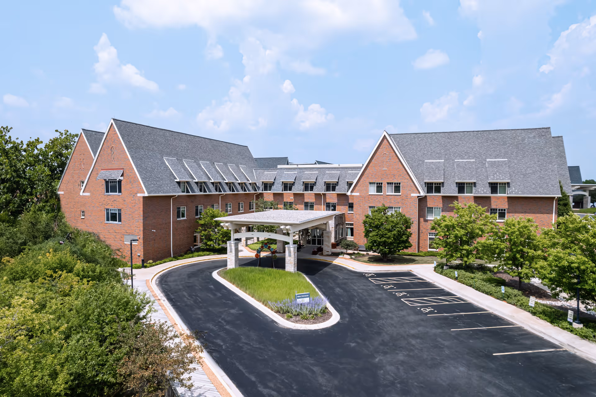 Front exterior of a brick senior living building with a covered entry drive and landscaped grounds.