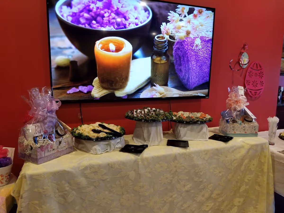 Buffet table with platters, gift baskets and a large TV displaying a candle and spa image against a red wall.