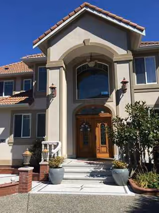 Front entrance of a beige senior living building with a wooden arched doorway.