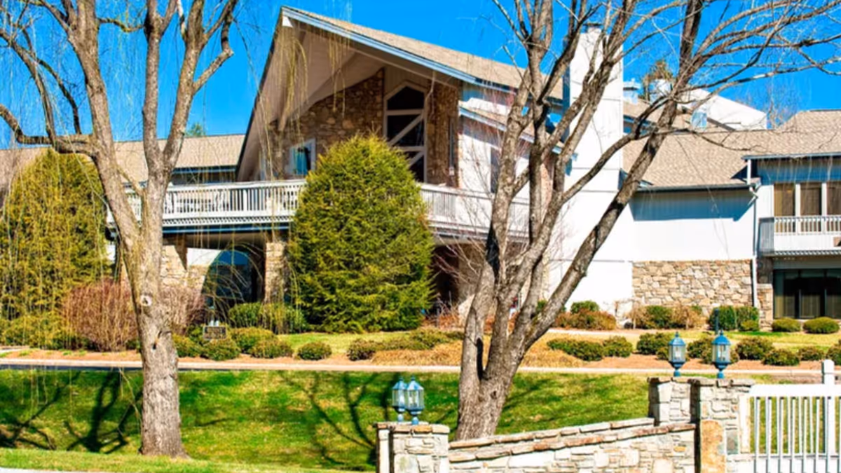 Exterior front of a senior living building with a stone facade, balcony, trees, and a landscaped grassy lawn.