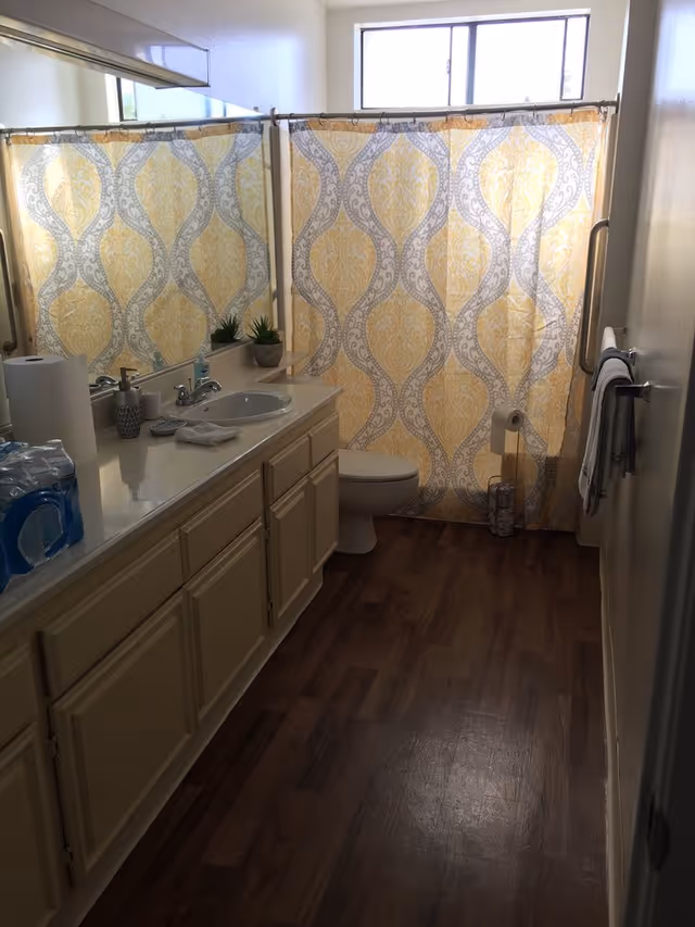 Bathroom with a long vanity and sink, toilet, and a yellow patterned shower curtain over the tub.