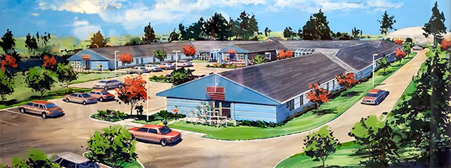 Illustration of a single-story extended health care facility named Heartwood Extended Health Care, surrounded by trees and greenery with a parking lot containing several cars and a driveway leading to the entrance.