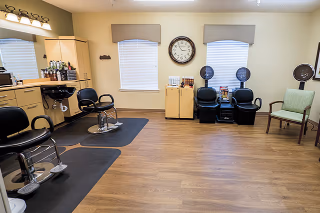 Interior view of a hair salon with styling chairs, a clock on the wall, and a waiting area with a green chair.