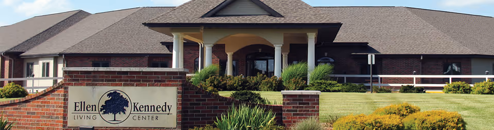 Brick entrance and landscaped front lawn with a sign reading 'Ellen Kennedy Living Center' in front of a single-story building.