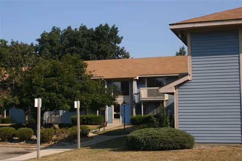 Exterior view of a blue retirement apartment building with a walkway and trimmed shrubs.