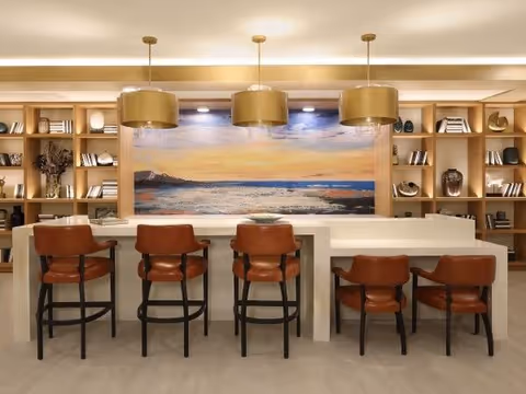 Modern communal dining/bar area with five leather barstools, pendant lights, and built-in shelving and artwork.
