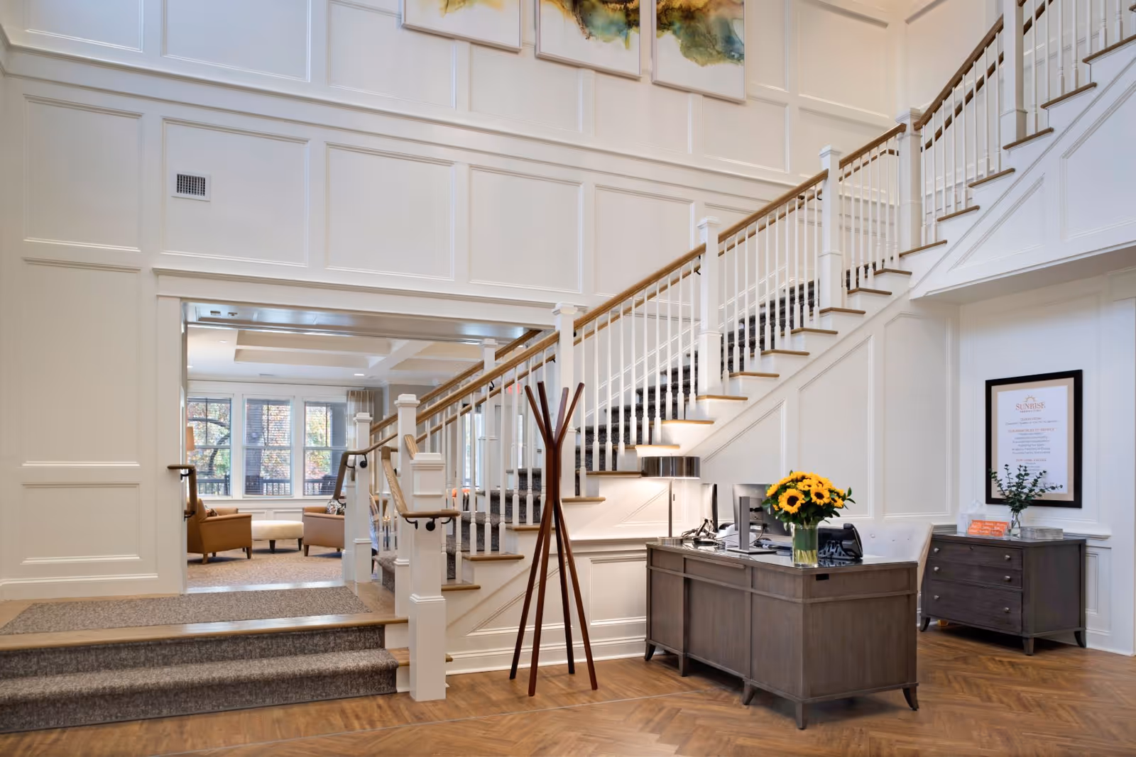 Bright, elegant interior lobby with a reception desk, vase of sunflowers, and a sweeping staircase.