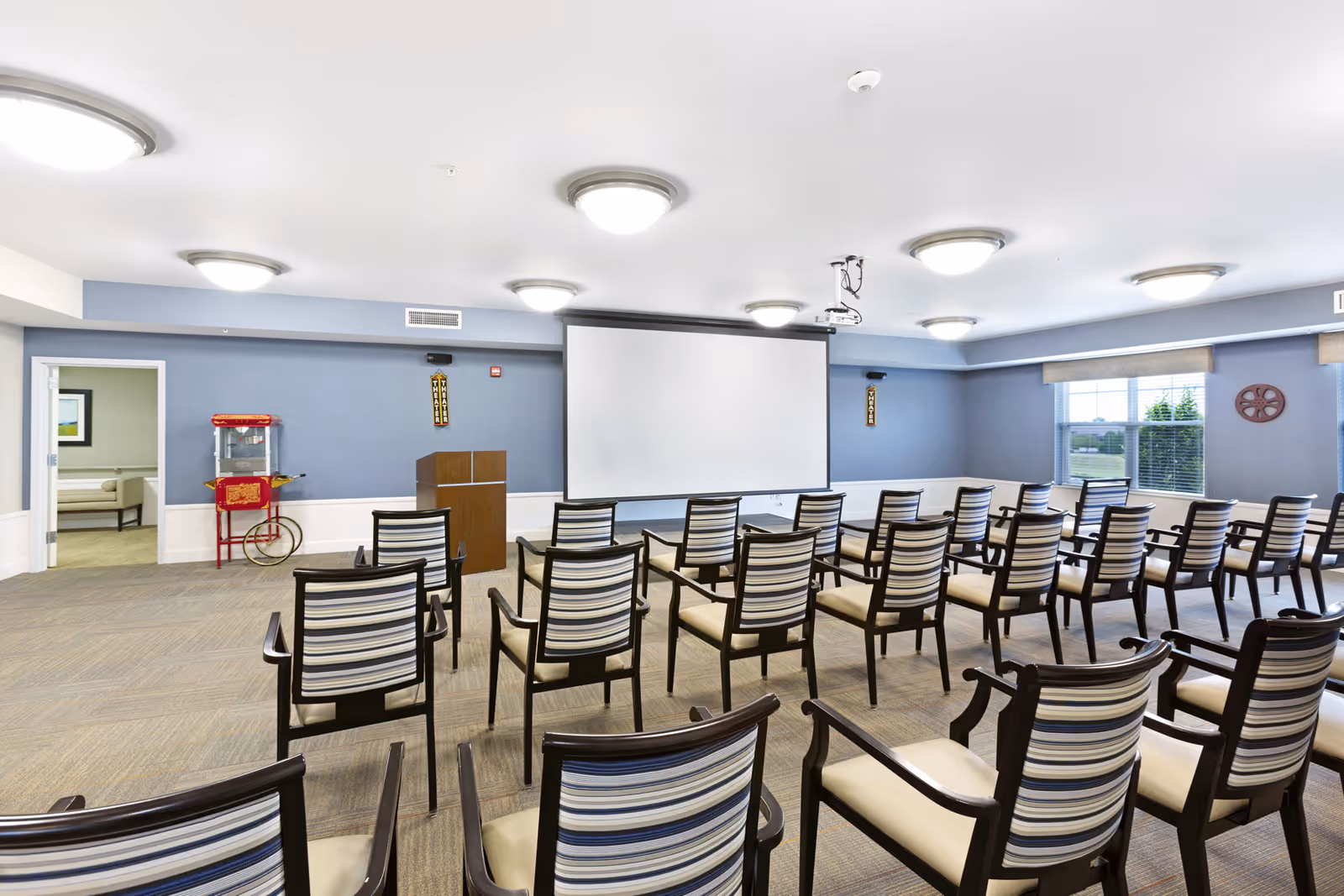 A meeting/activity room with rows of striped chairs facing a projector screen and podium.