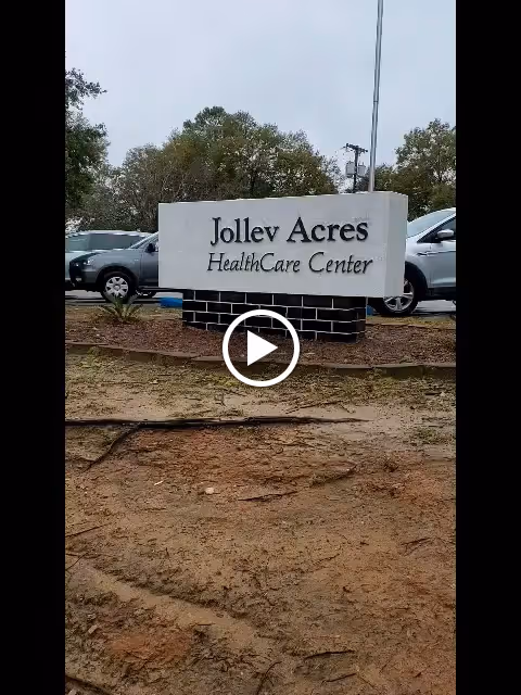 Outdoor view of a sign for Jolley Acres HealthCare Center with cars parked in the background and trees behind the sign.