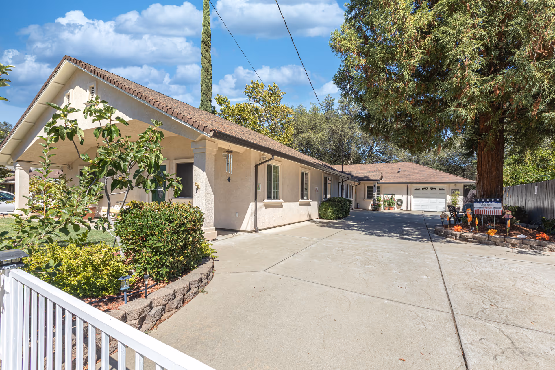 Front exterior of a single-story senior living building with a wide concrete driveway, garage, and landscaped yard.