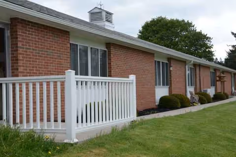 Exterior view of a brick senior living facility with white railings and a green lawn.