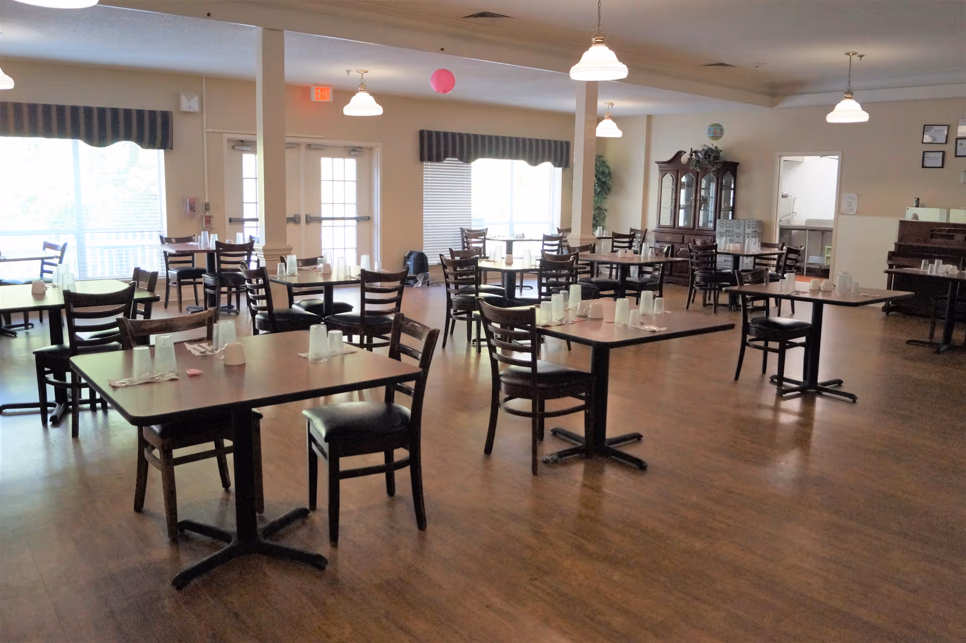 Empty dining room with multiple tables and chairs on a wood floor, each place set with cups and utensils.