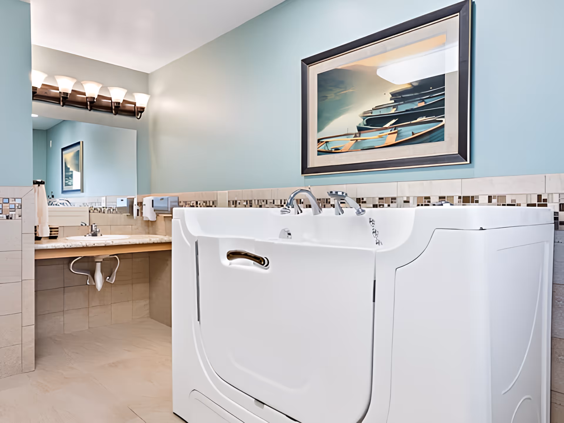 A clean and modern bathroom featuring a walk-in bathtub with a door, chrome faucets, and a tiled backsplash. The walls are painted light blue, and there is a large mirror above a beige countertop with a sink. A framed picture of boats is hung on the wall above the bathtub.