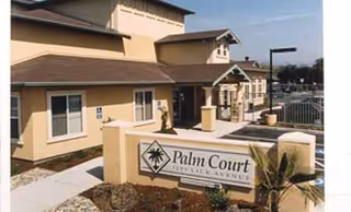 Exterior view of Palm Court Senior Homes with entrance sign and walkway.