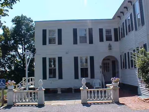 White two-story senior living facility exterior with black shutters and a brick entry
