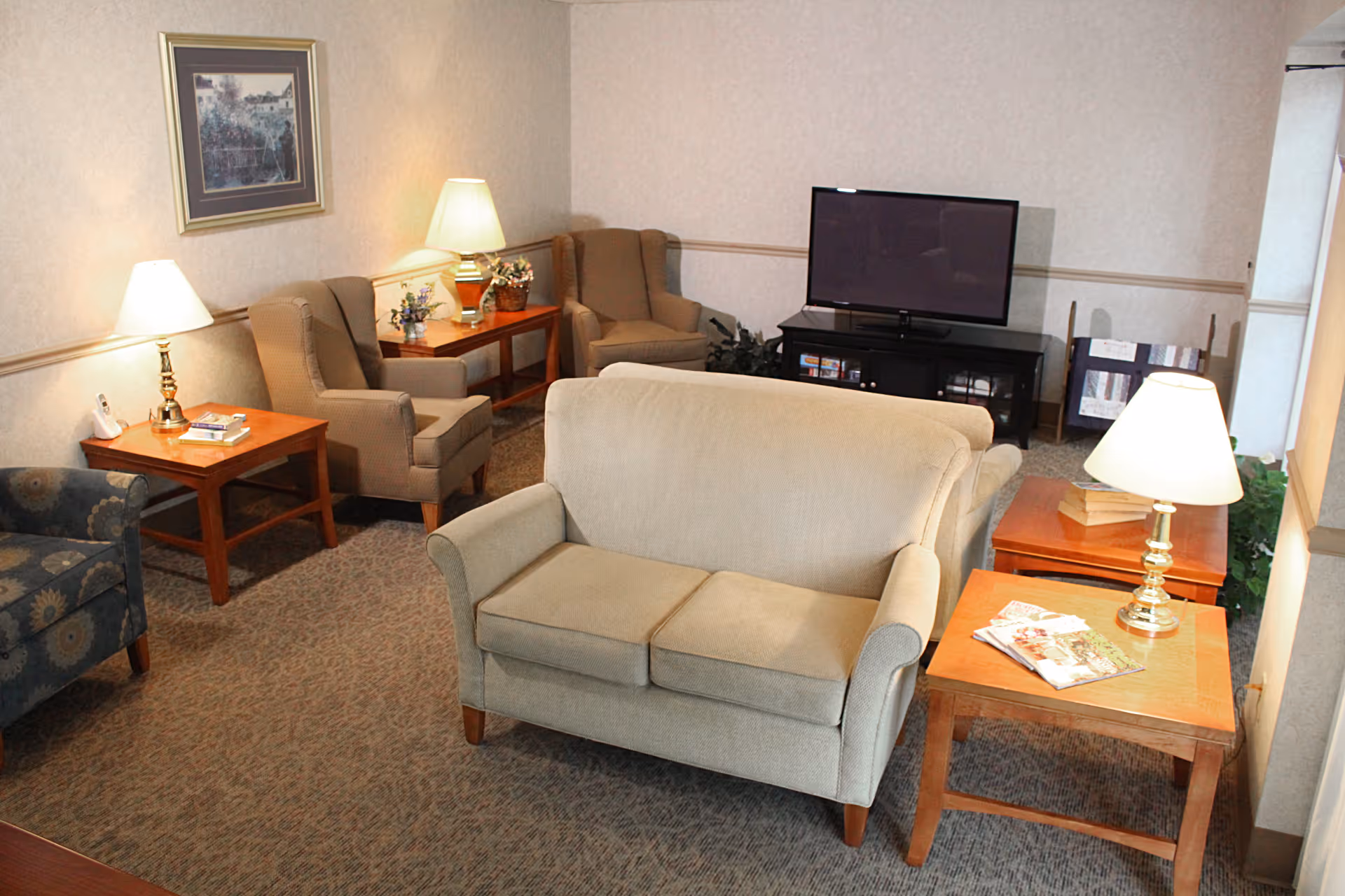 Cozy sitting room with a loveseat and armchairs, side tables with lamps, and a TV on a stand.