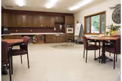 Communal dining area with tables and chairs and a long kitchen counter with cabinets along the back wall.