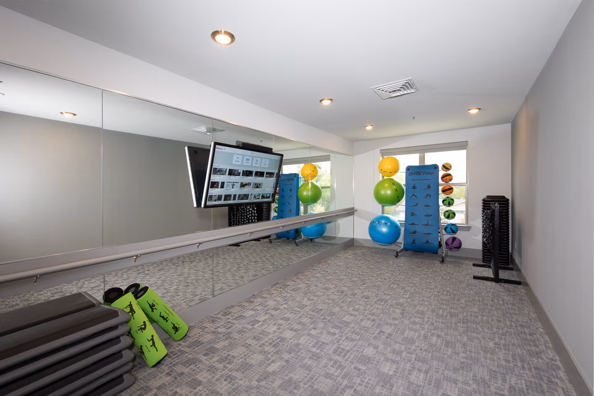 Small fitness/stretching room with mirrored wall, wall-mounted TV, exercise balls, step platforms and mats.
