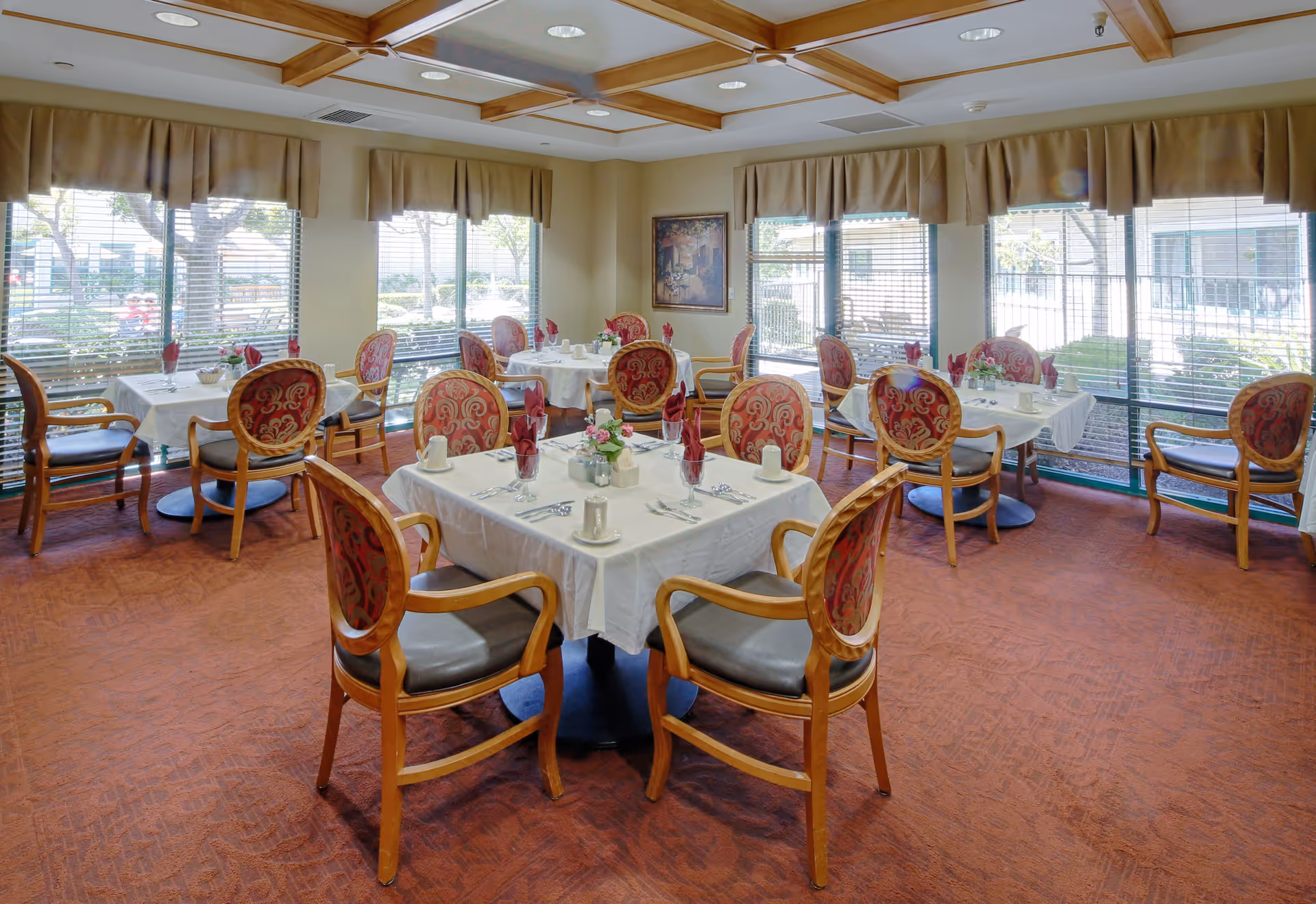 Dining room with several set tables, patterned upholstered chairs, and large windows overlooking the grounds.