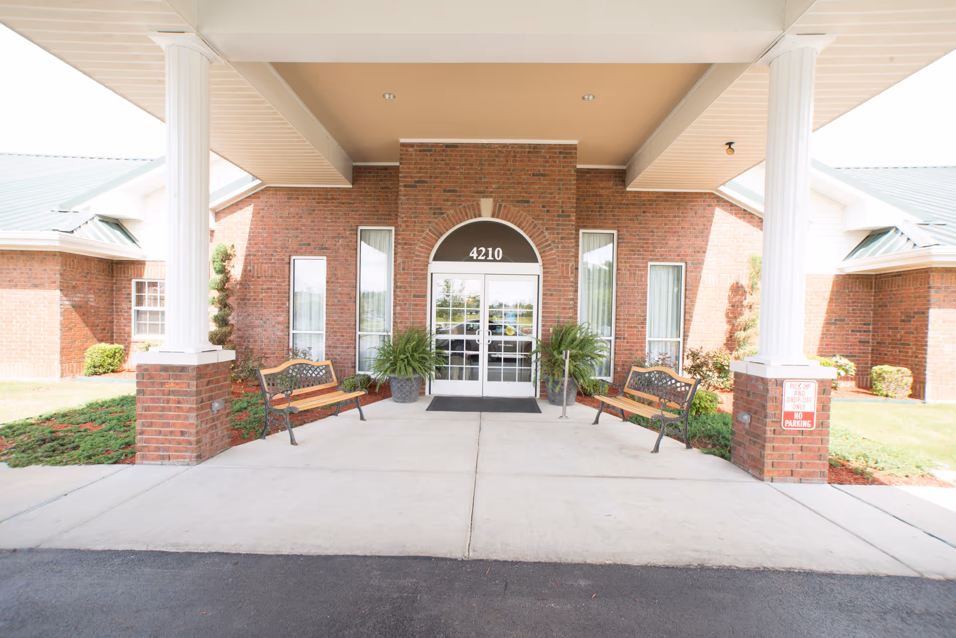 Covered brick entrance with columns, benches, potted plants and glass doors numbered 4210.