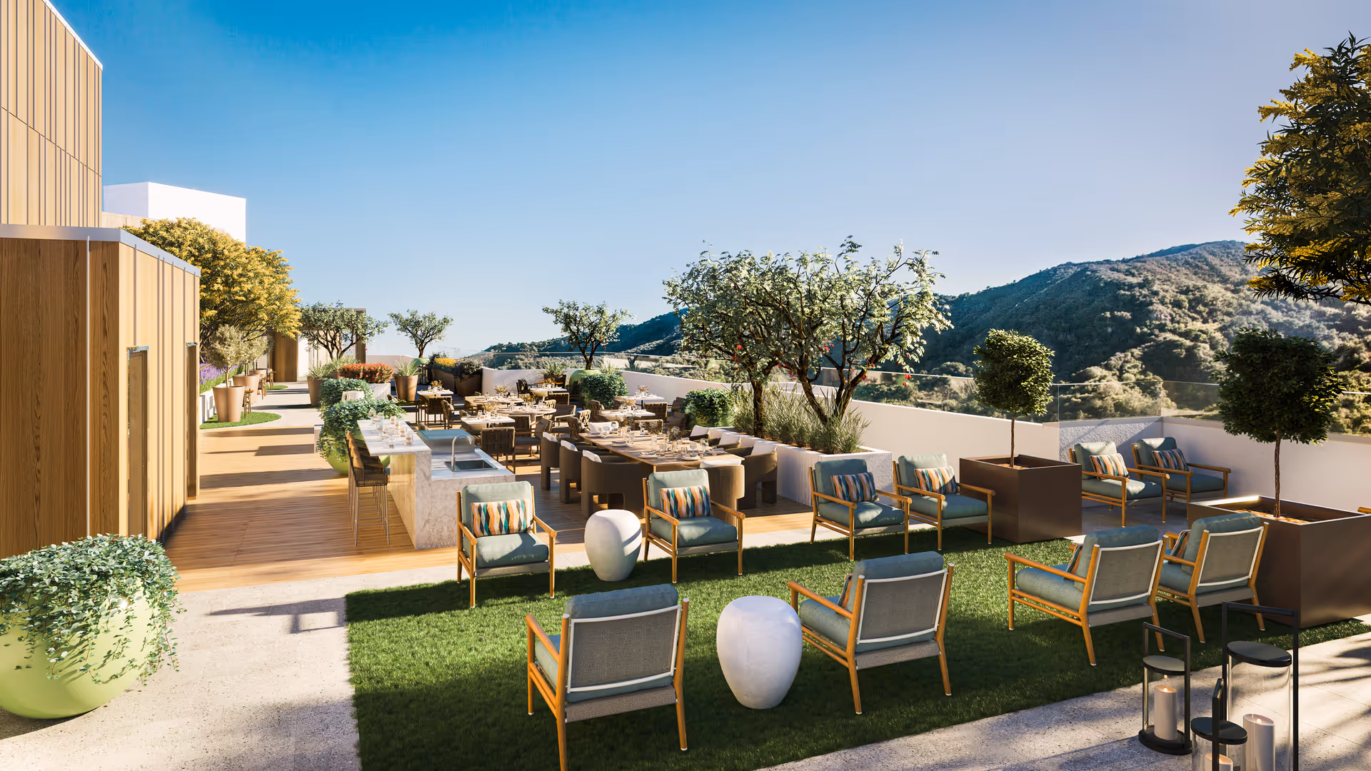 Outdoor patio area at Ciela Senior Living featuring multiple seating arrangements with cushioned chairs and small tables on a grassy and wooden deck. There are potted plants and trees around the space, with a scenic view of mountains under a clear blue sky.