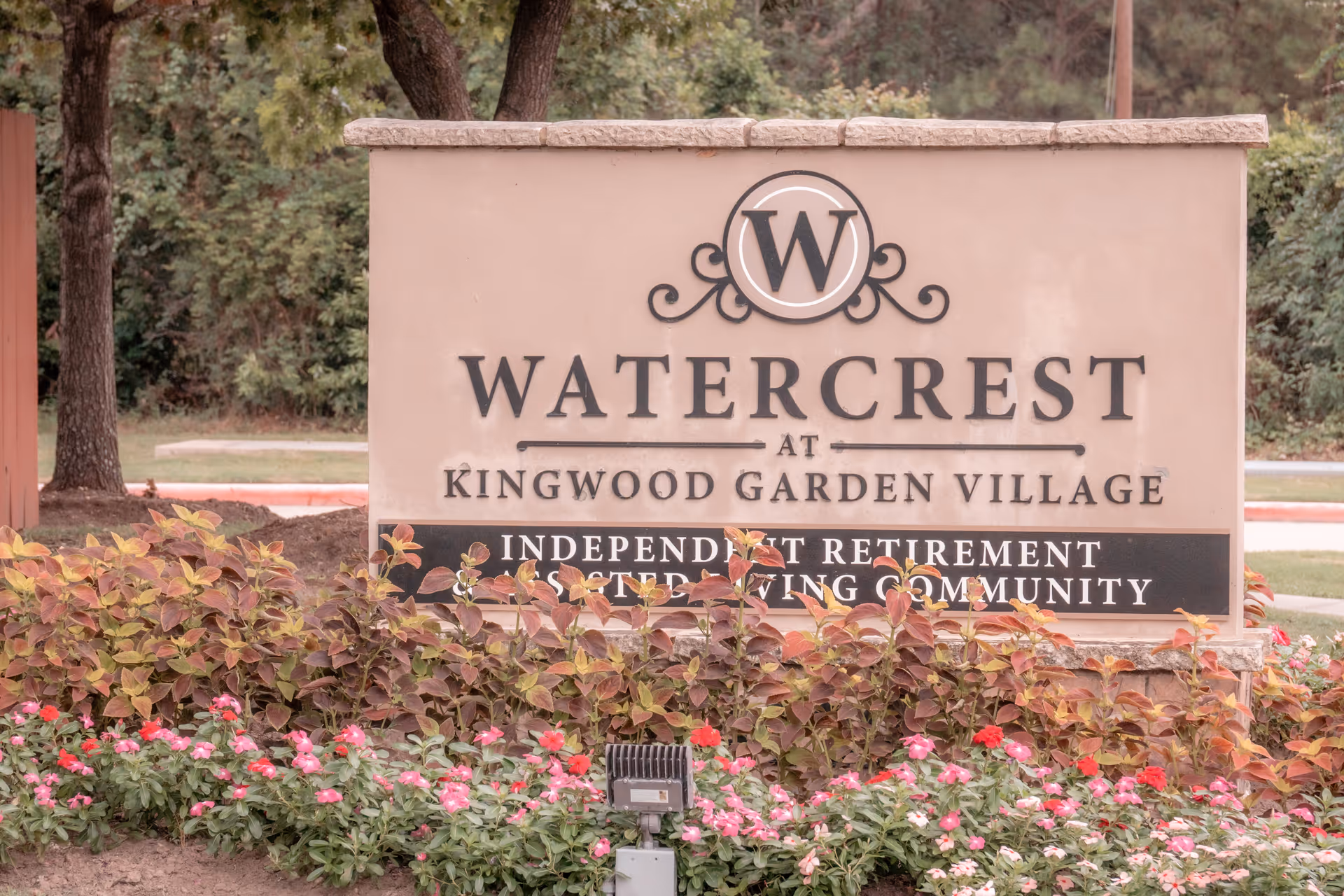 Outdoor stone entrance sign reading "WATERCREST at Kingwood Garden Village" set among flowers and landscaping.