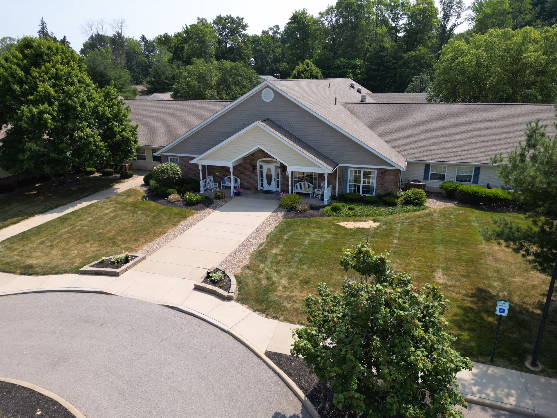 Aerial view of the front entrance of a single-story memory care facility with a circular drive, walkway, and landscaped lawn.