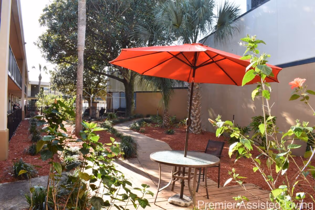 Courtyard with a red patio umbrella over a round table and chairs next to a wooden walkway and landscaped plants.