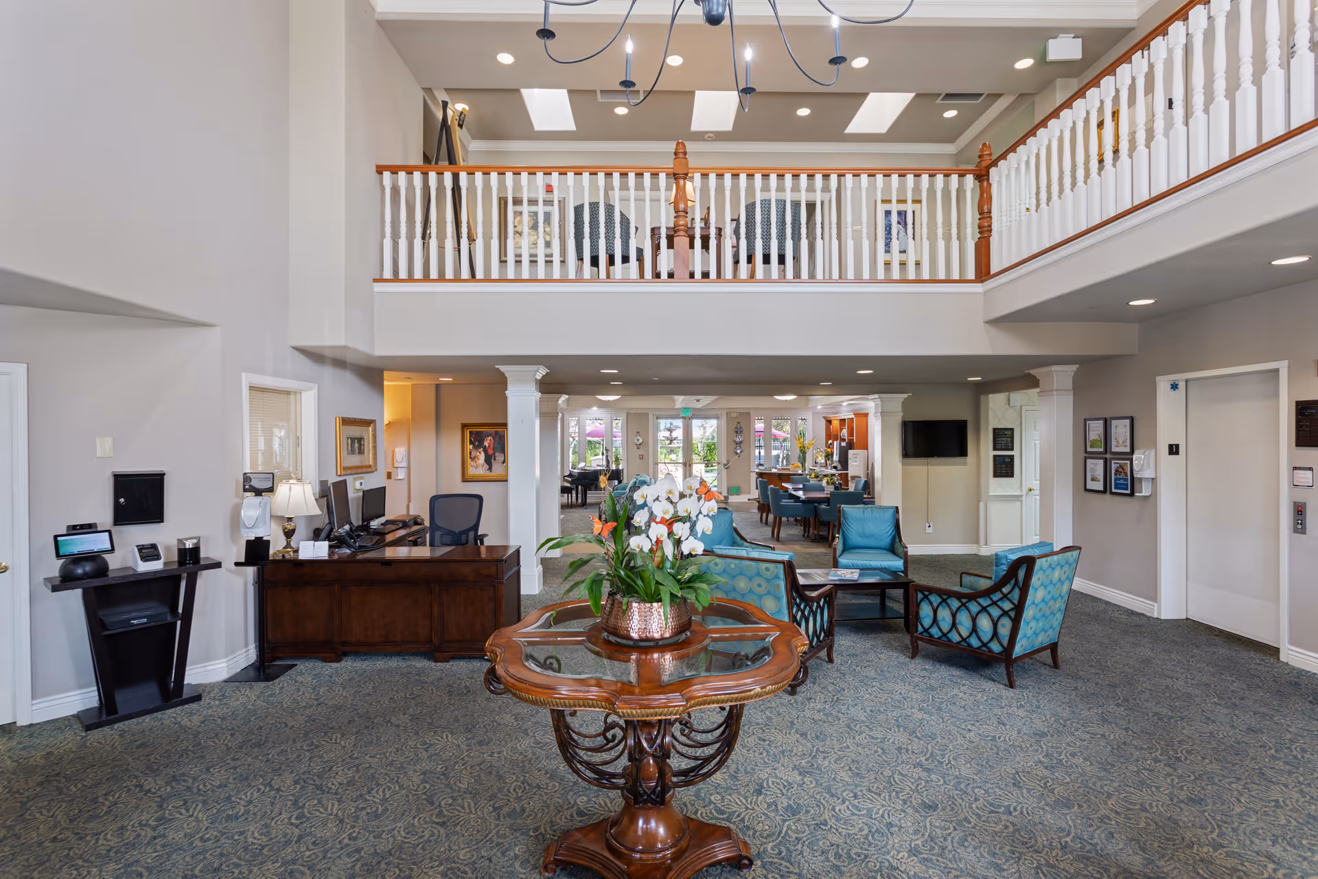 Spacious two-story lobby and reception area with a central table of flowers, seating group, front desk, and an upstairs balcony railing.