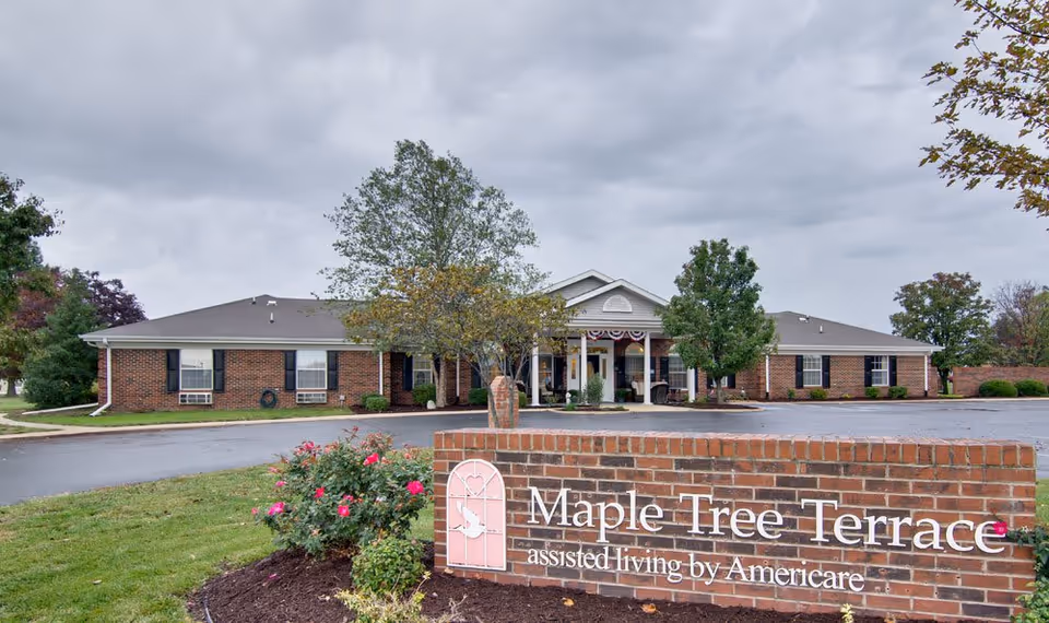 Front view of a single-story brick assisted living building with a portico and a brick sign reading "Maple Tree Terrace" in the foreground.