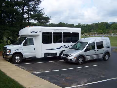 Two white vehicles, a bus and a van, parked in a paved lot with grassy surroundings.