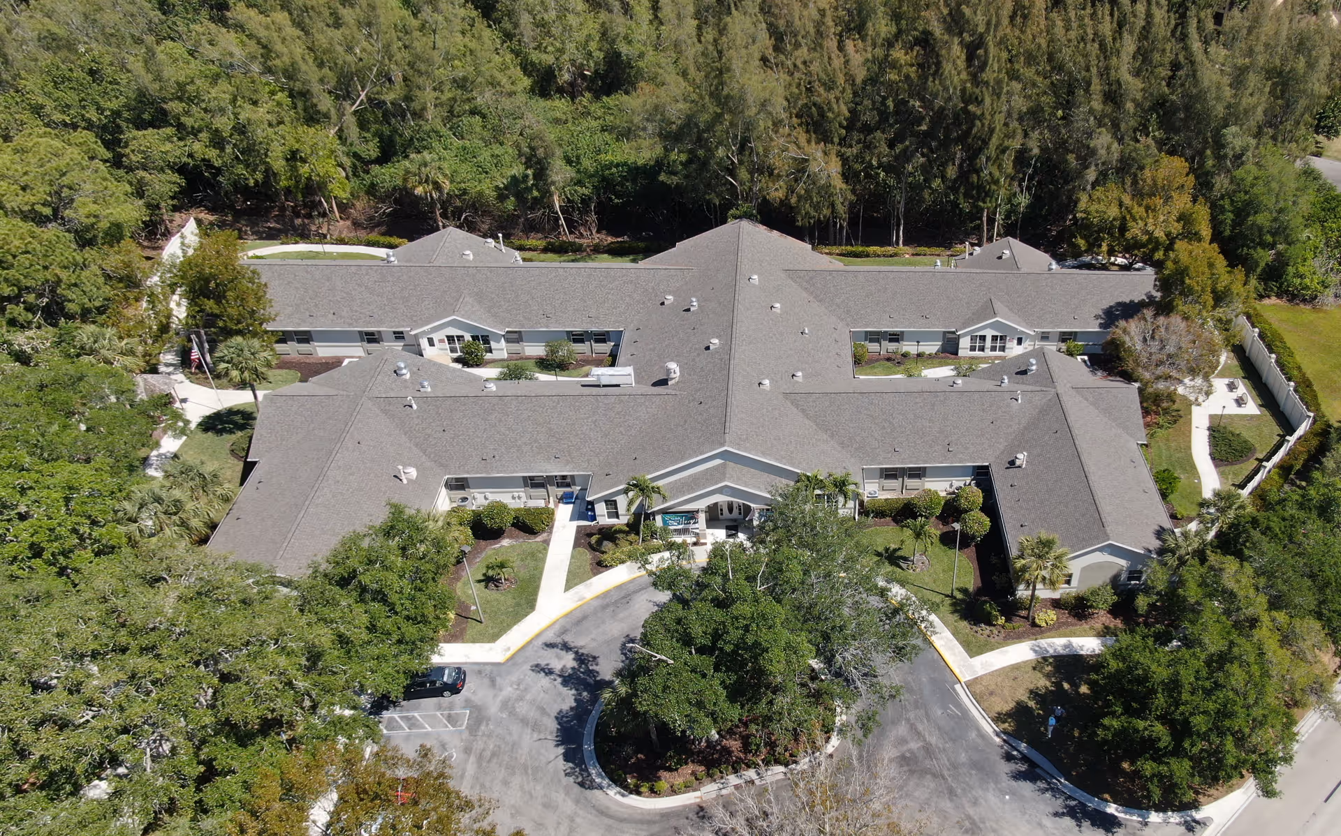 Aerial view of a single‑story memory care building with a central entrance, circular driveway and surrounding trees.