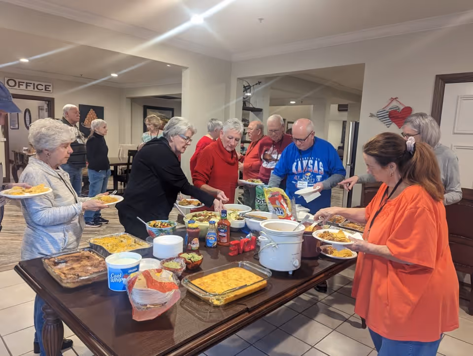 Several older adults serve themselves from a buffet spread on a table in a community dining area.