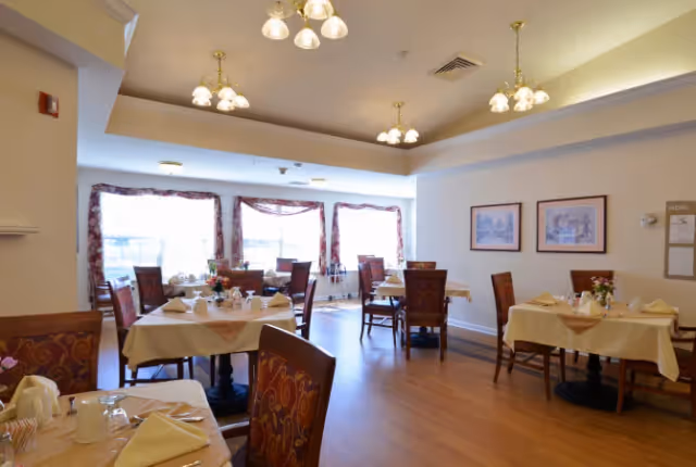 Bright dining room with multiple set tables, chairs, chandeliers, and large windows.