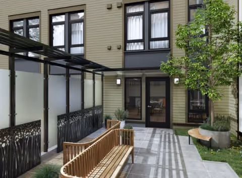 Outdoor courtyard area at Empress Senior Living at Laurelhurst featuring wooden benches, a small tree in a planter, frosted glass panels with decorative metalwork, and a building facade with large windows and a glass door.