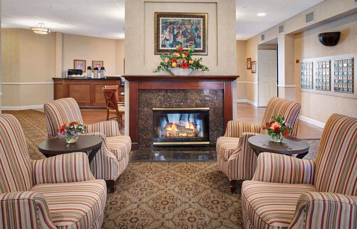 Cozy common seating area with striped armchairs and small tables arranged around a lit fireplace and floral arrangements.