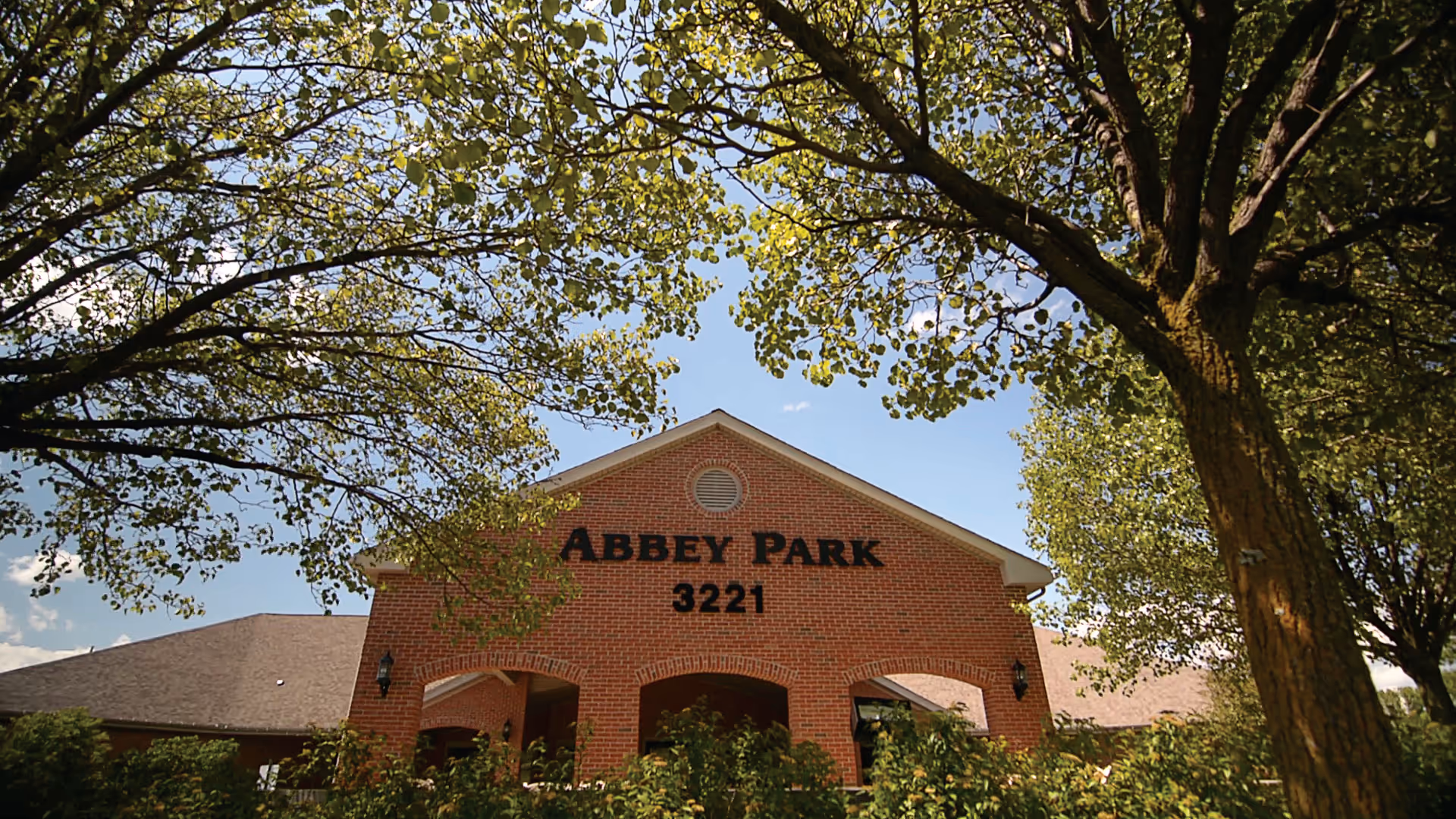 Brick front entrance of Abbey Park with the number 3221 visible, framed by trees under a blue sky.