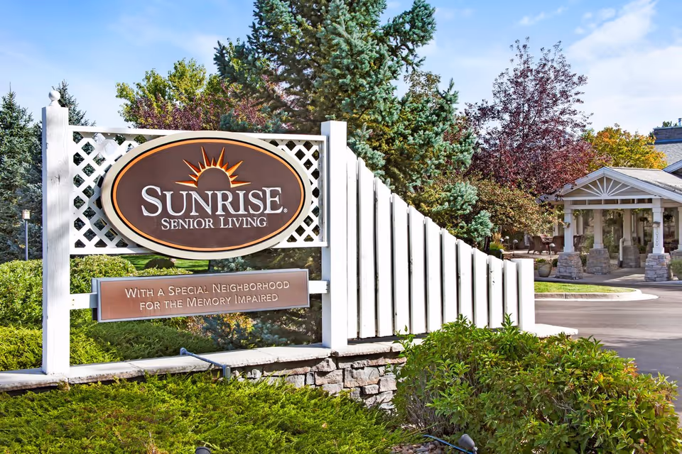 Entrance sign for Sunrise Senior Living beside landscaped grounds and the facility's front drive and portico.