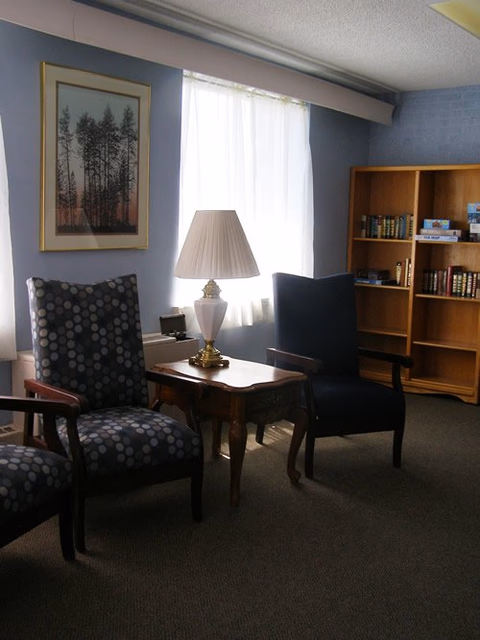 Interior living room in Cambridge Court with chairs, a lamp, and a bookshelf.