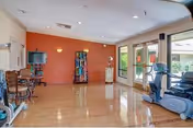 Spacious fitness/activity room with hardwood floor, exercise machines, chairs and large glass doors opening to an outdoor area.