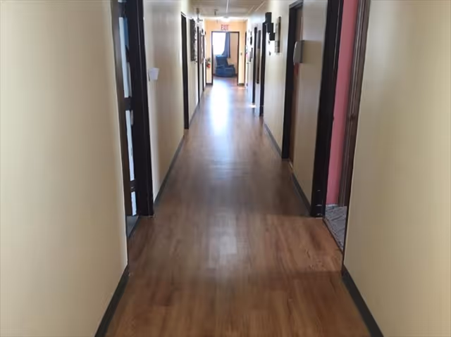 Long interior hallway with wood-look flooring and multiple doorways on both sides leading toward an exit sign.