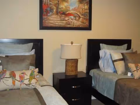 Two twin beds with a shared nightstand and lamp in a neutral-toned bedroom.
