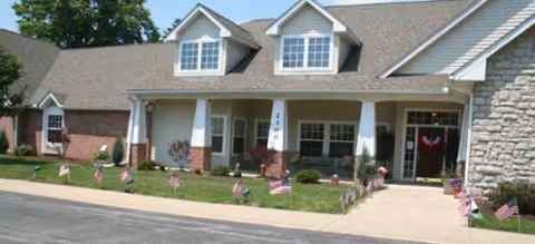 Front entrance of a senior living facility with a green lawn and small American flags.