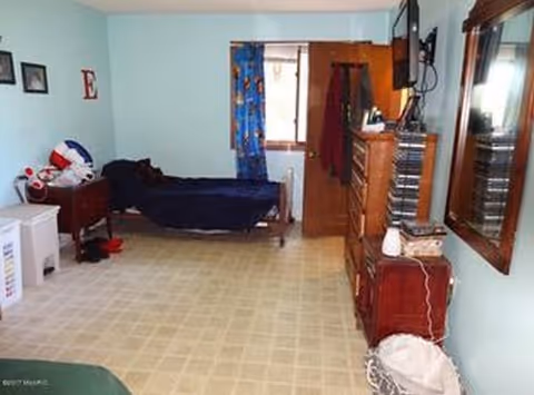 A bedroom in a senior living facility featuring a bed, dresser, TV, and window.