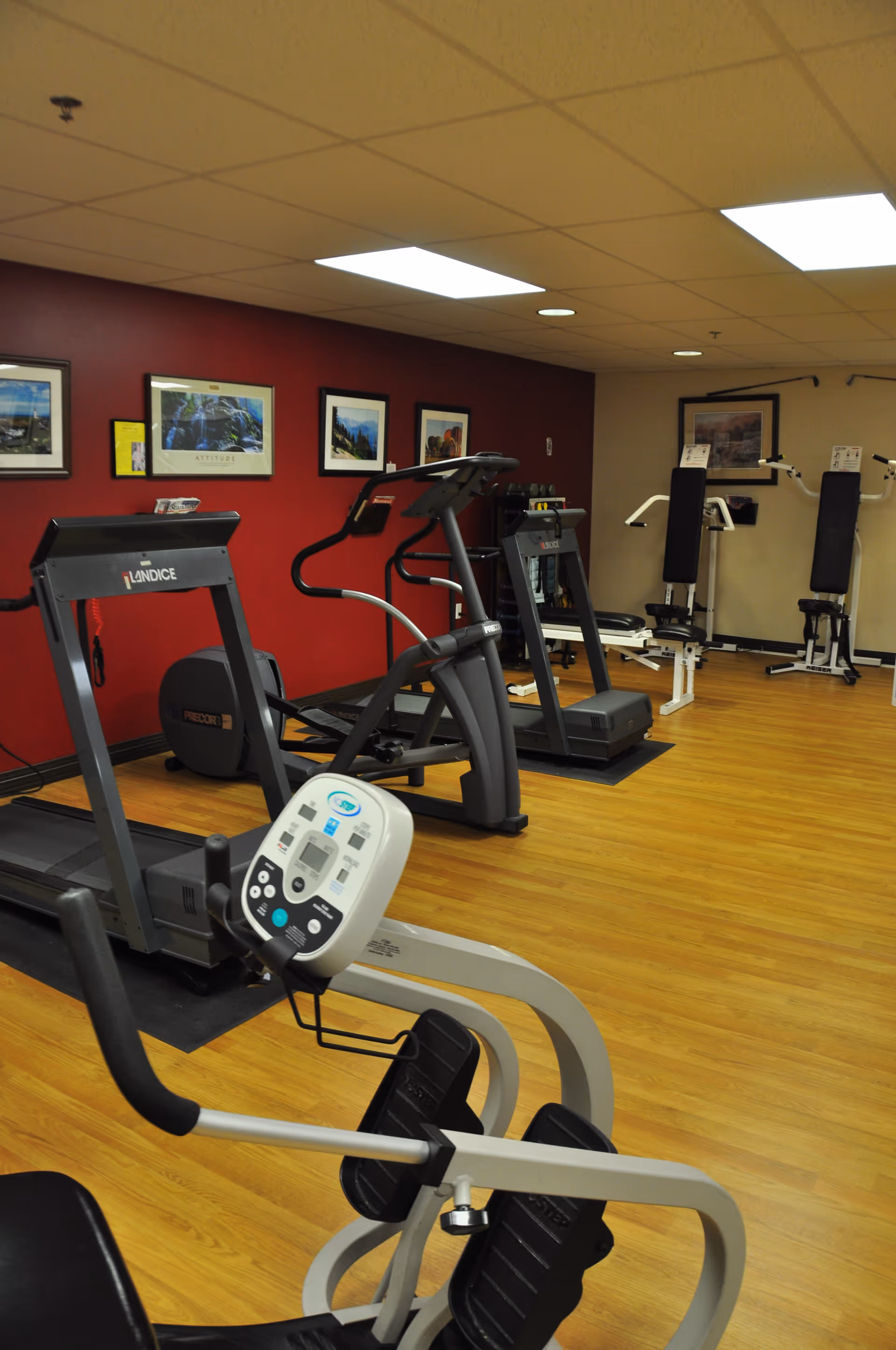 Small fitness room with treadmills, an elliptical and strength machines against a red wall with framed pictures.