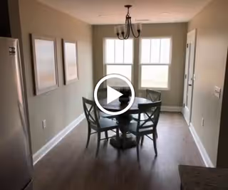 Dining area with a round table and four chairs beneath a chandelier in a bright room with two windows.